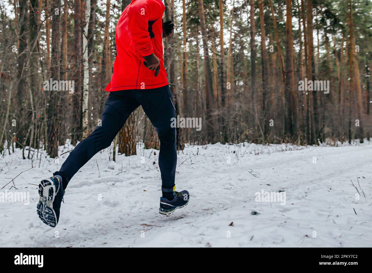 Running Trail Race für Männer in roter Sportjacke, Jogging im verschneiten Wald bei kaltem Wetter Stockfoto