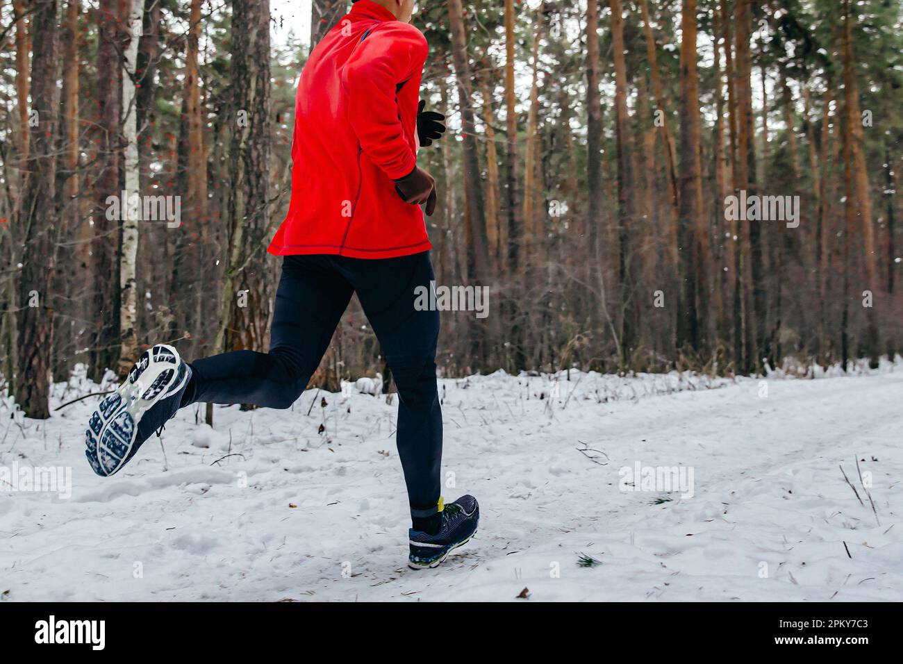 Männlicher Läufer Laufstreckenrennen in Winterkleidung, Mann joggt bei kaltem Wetter im verschneiten Wald Stockfoto