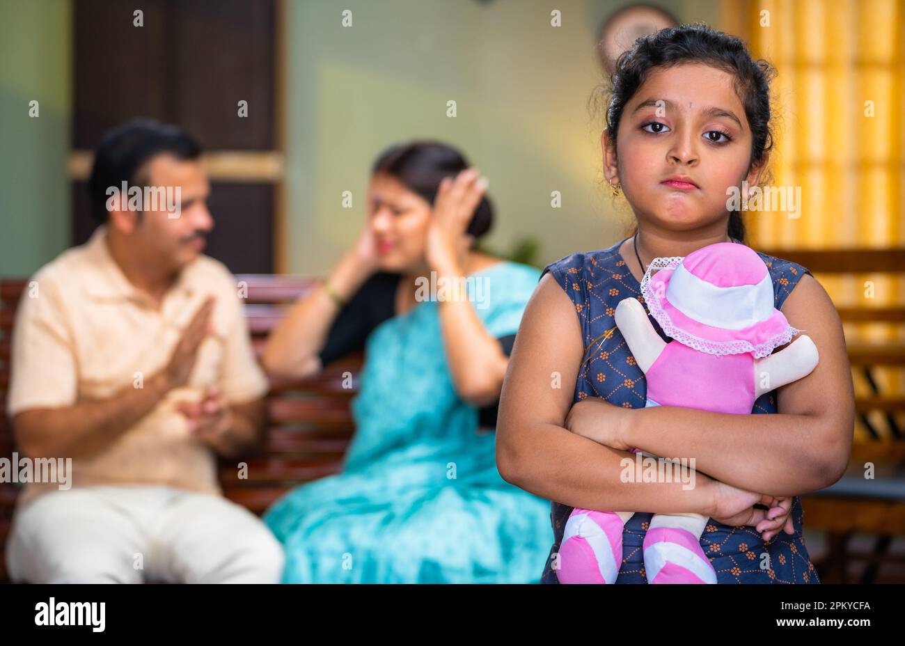 Stegfokussierung eines traurigen Kindes mit Puppe vorne, die Eltern zu Hause auf dem Sofa schreit und sich streitet - Konzept von Depression, Unschuld und Beziehungsgeist Stockfoto