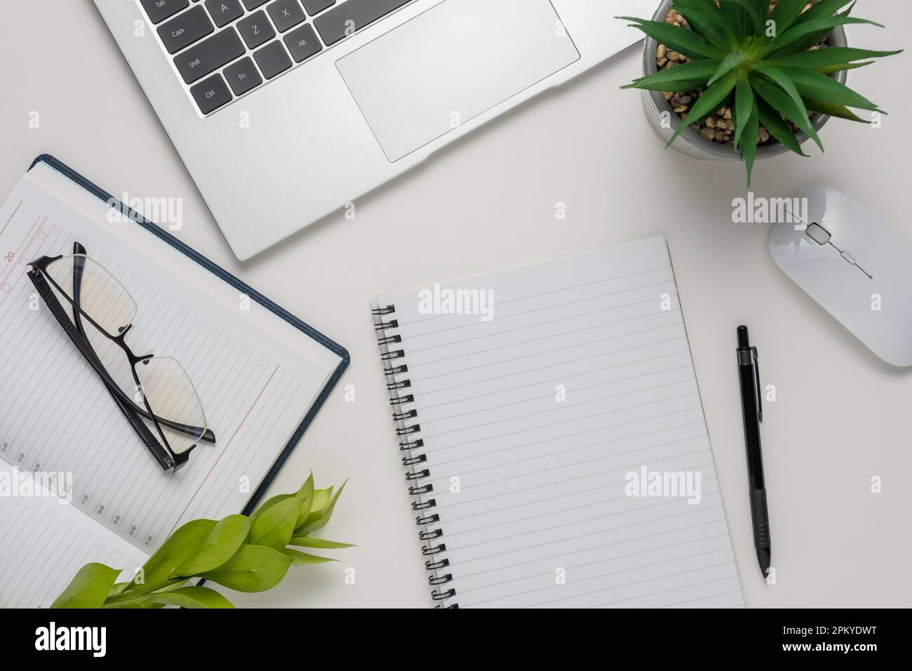 Arbeitsplatz mit leerem Notebook, Laptop, Büromaterial, grünem Blatt und Brille auf weißem Hintergrund. Flach liegender Schreibtisch mit Blick von oben. Stockfoto