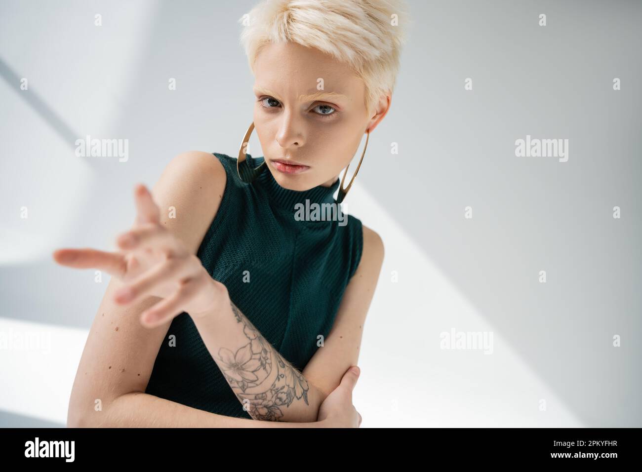 Tätowierte Albino-Frau mit heller Geste, während sie auf grauen Hintergrund in die Kamera schaut Stockfoto Tätowierte Albino-Frau mit heller Geste, während sie auf grauen Hintergrund in die Kamera schaut Stockfoto