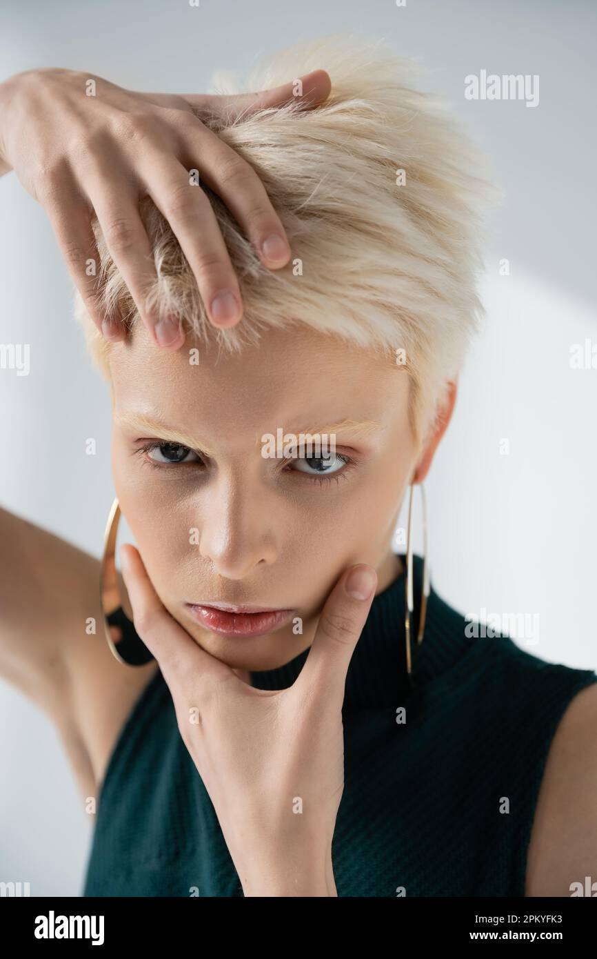 Junges Albino-Modell mit hellhäutigem Gesicht mit Händen beim Posen auf Grau Stockfoto Junges Albino-Modell mit hellhäutigem Gesicht mit Händen beim Posen auf Grau Stockfoto
