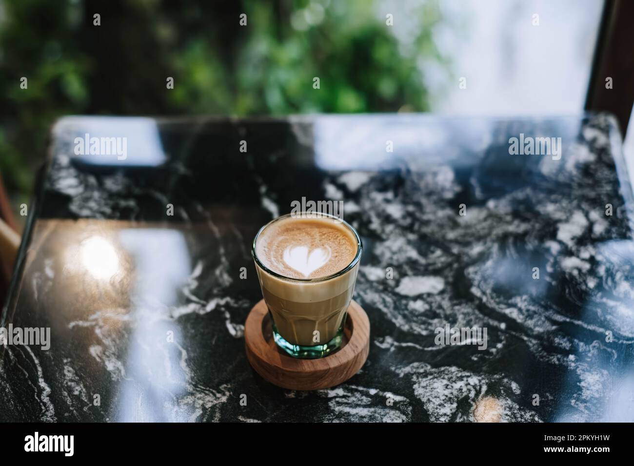 Minimalistischer Kaffee-Latte mit hölzerner Untersetzer auf Marmortisch. Verschwommener Hintergrund Stockfoto