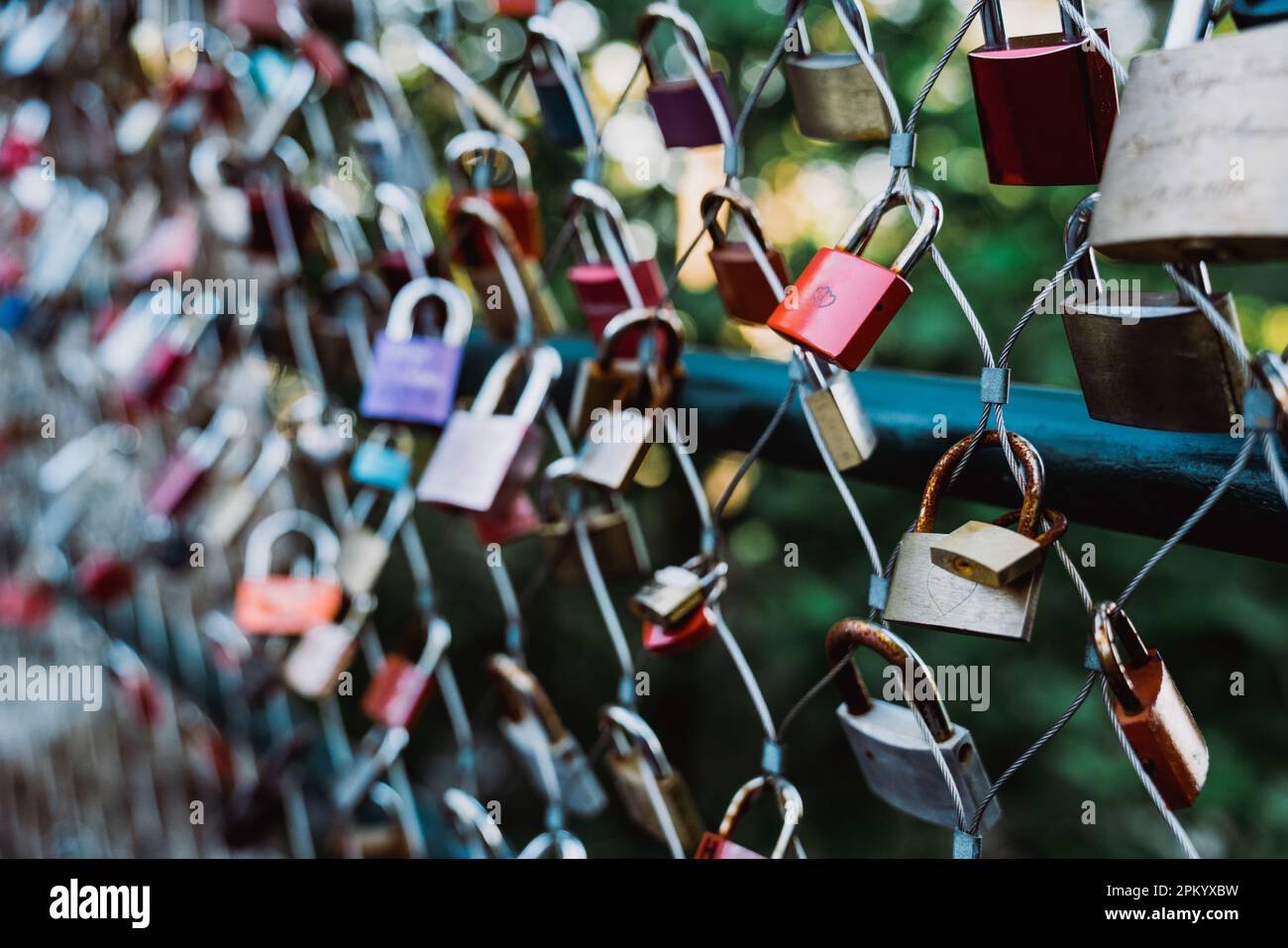 Haufen von verschiedenen Liebe Vorhängeschlösser hängen auf Netzzaun auf Verschwommener Hintergrund des grünen Parks Stockfoto