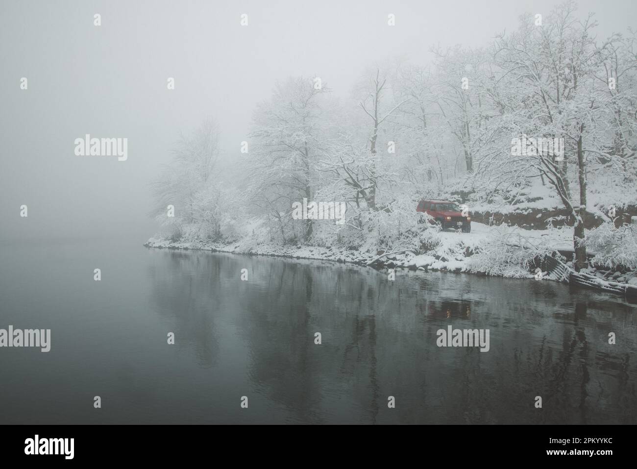 Eine unberührte Winterszene mit einem ruhigen See, umgeben von hohen, schneebedeckten Kiefern Stockfoto