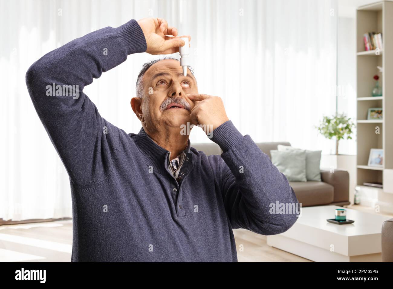 Reifer Mann mit Augentropfen zu Hause im Wohnzimmer Stockfoto