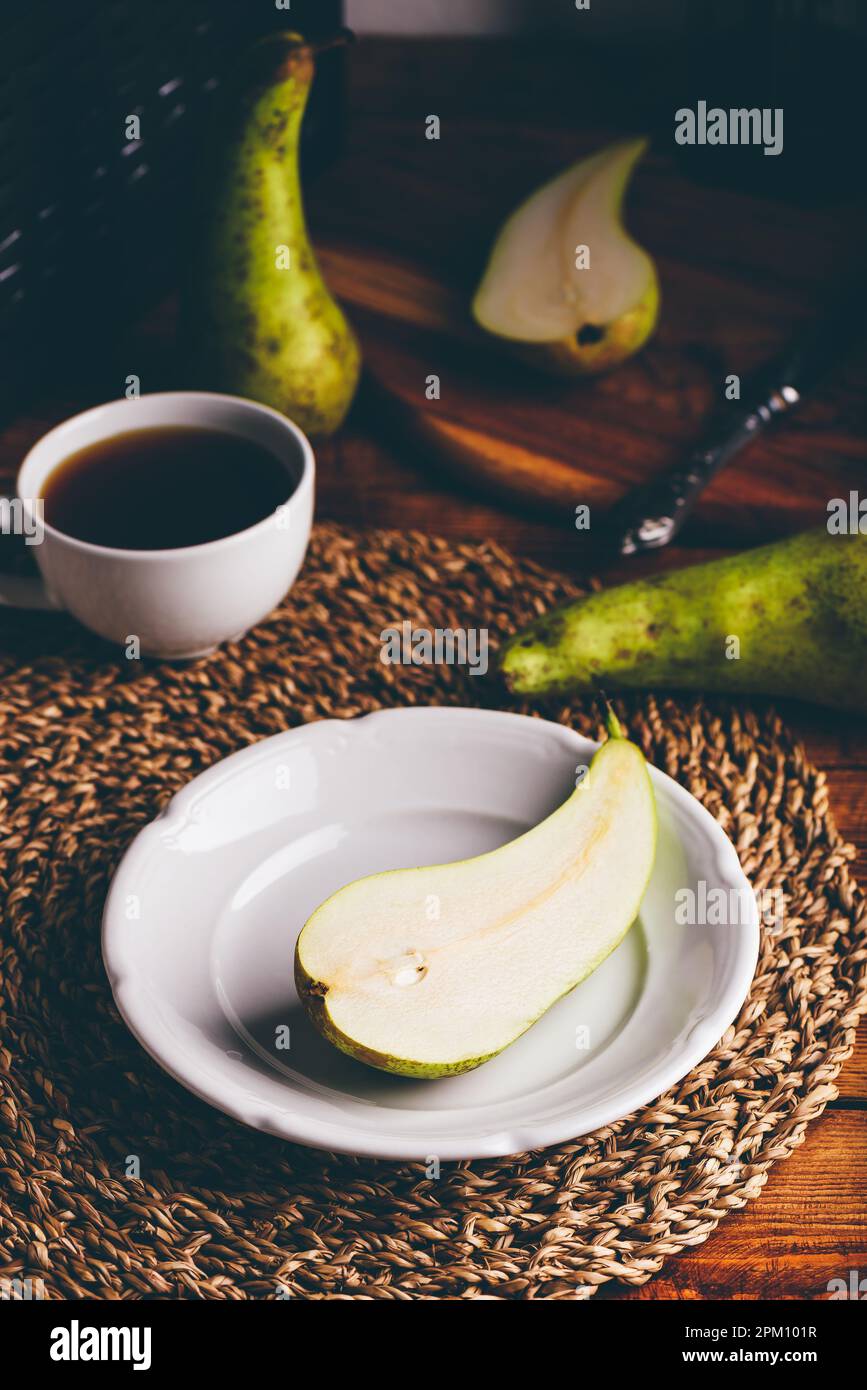Die Hälfte der grünen Birne auf weißem Teller und Tasse Kaffee Stockfoto