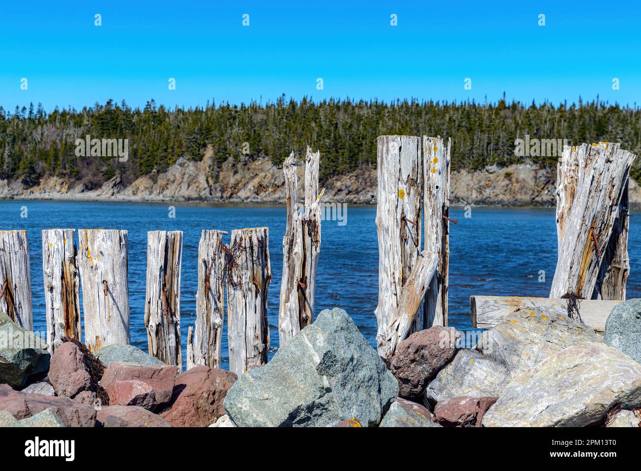 Zerschmetterte und zerbrochene Holzmauer hält einen Steinbruch. Wasser dahinter und Bäume weiter dahinter. Stockfoto