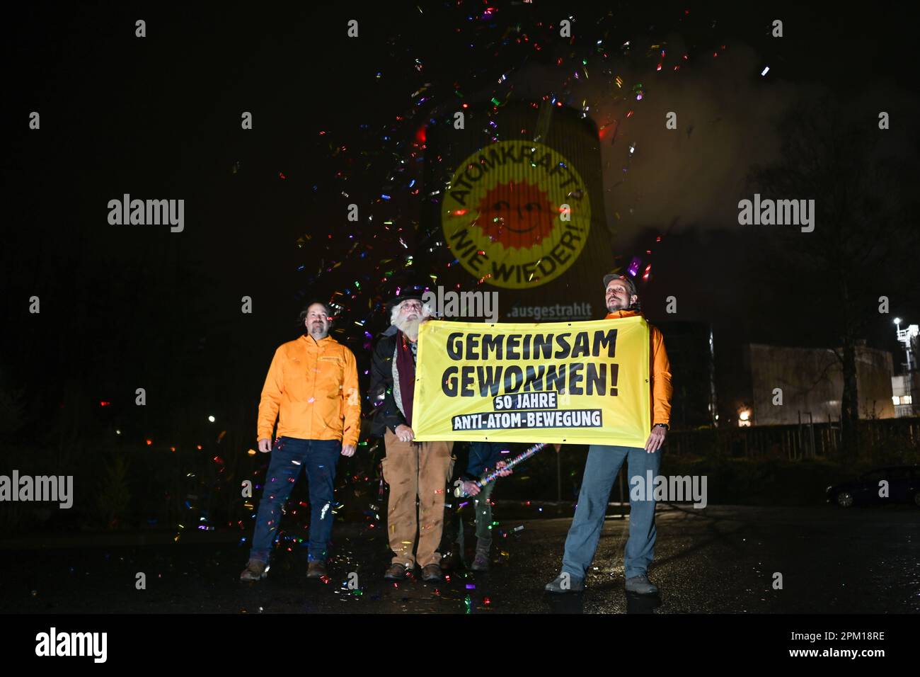 Lingen, Deutschland. 10. April 2023. Aktivisten der Anti-Atombewegung halten ein Banner und schießen Konfetti in die Luft, während sie eine große Anti-Atomsonne auf den Kühlturm des Emsland Kernkraftwerks projizieren. Der Anlass ist die Abschaltung des letzten Kernkraftwerks am 15. April. Ursprünglich aus Dänemark, ist die rote antinukleare Sonne auf gelbem Hintergrund zum weltweiten Symbol dieser Bewegung geworden. Kredit: Lars Klemmer/dpa/Alamy Live News Stockfoto