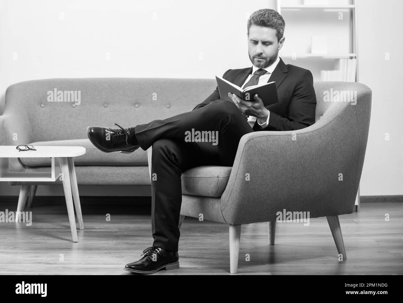 Reifer Geschäftsmann in Anzug sitzen im Büro Buch lesen Stockfoto