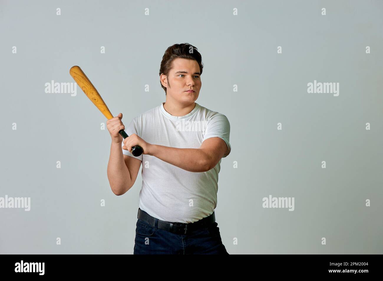 Ein Mann mit einem Schläger in der Hand schwingt auf grauem Hintergrund Stockfoto