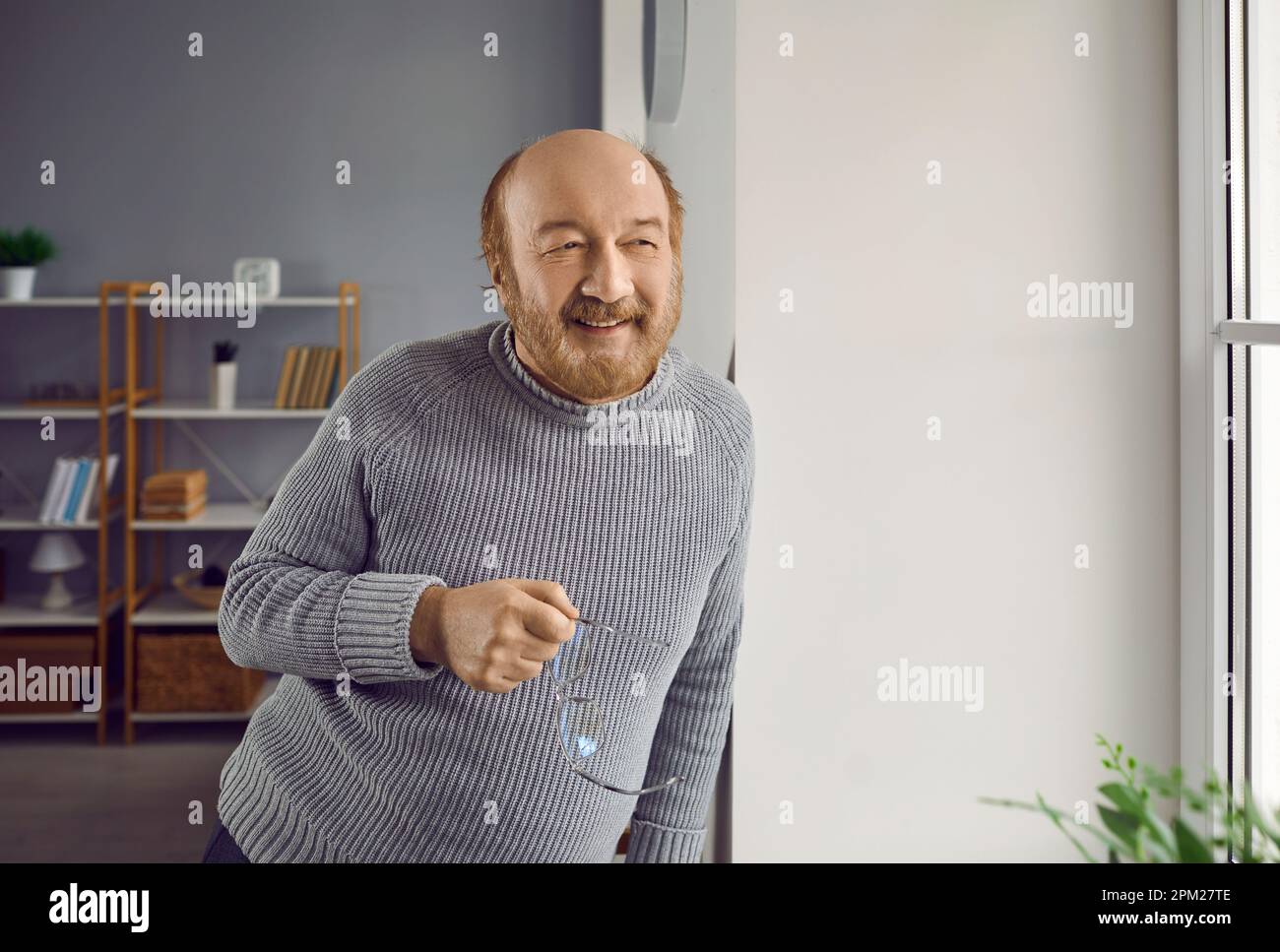 Porträt eines glücklichen, fröhlichen älteren Rentners, der zu Hause am Fenster steht Stockfoto