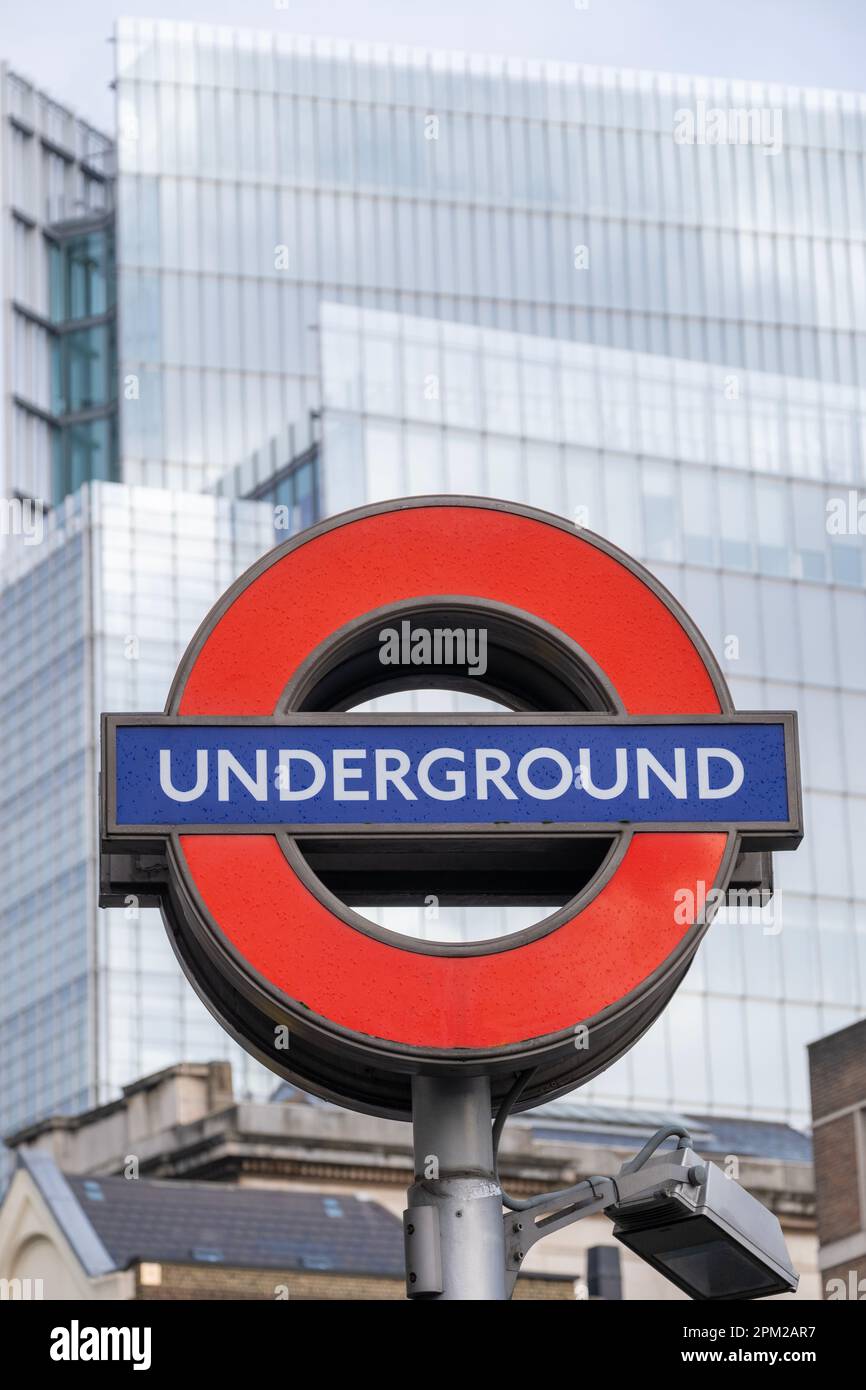 Blick aus dem niedrigen Winkel auf das berühmte „London Underground Roundel“-Schild vor dem Hintergrund moderner Bürogebäude im Zentrum von London, Großbritannien. Stockfoto