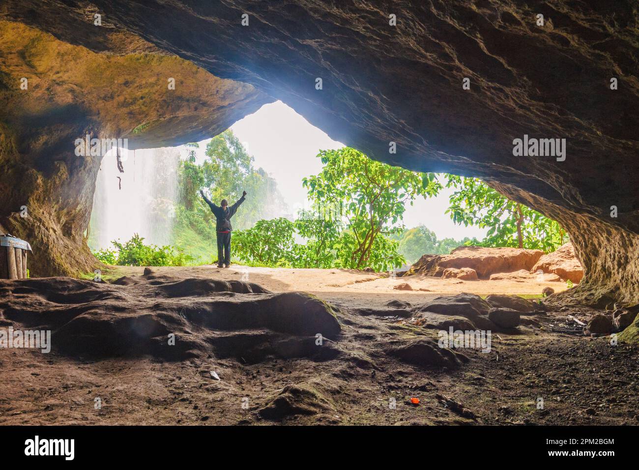 Rückansicht eines Mannes in einer Höhle vor einem Wasserfall in Sipi Falls, Kapchorwa, Uganda Stockfoto