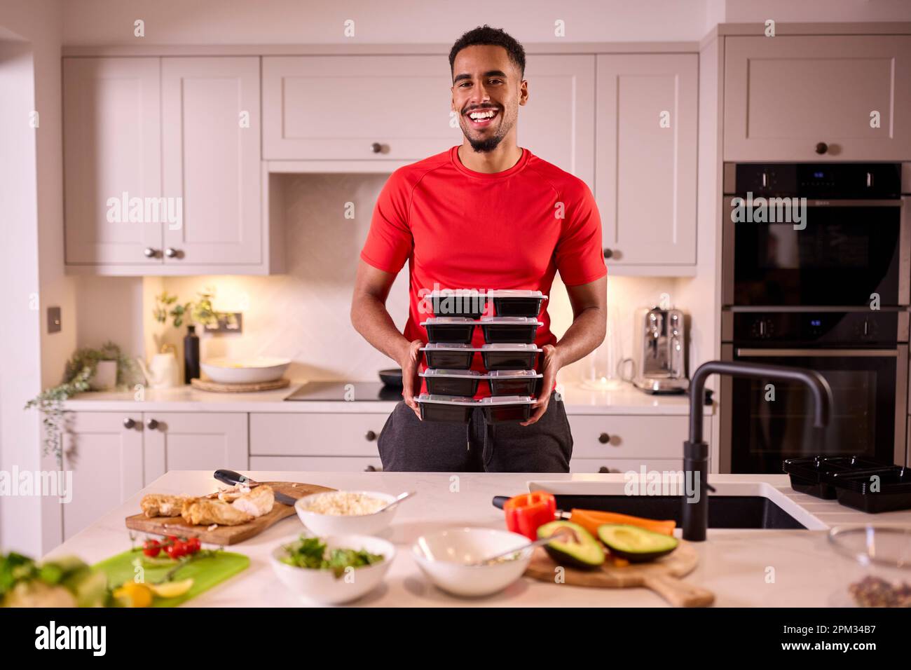 Porträt Des Mannes In Der Küche Mit Fitness-Kleidung, Die Eine Charge Gesunder Mahlzeiten Für Den Gefrierschrank Macht Stockfoto