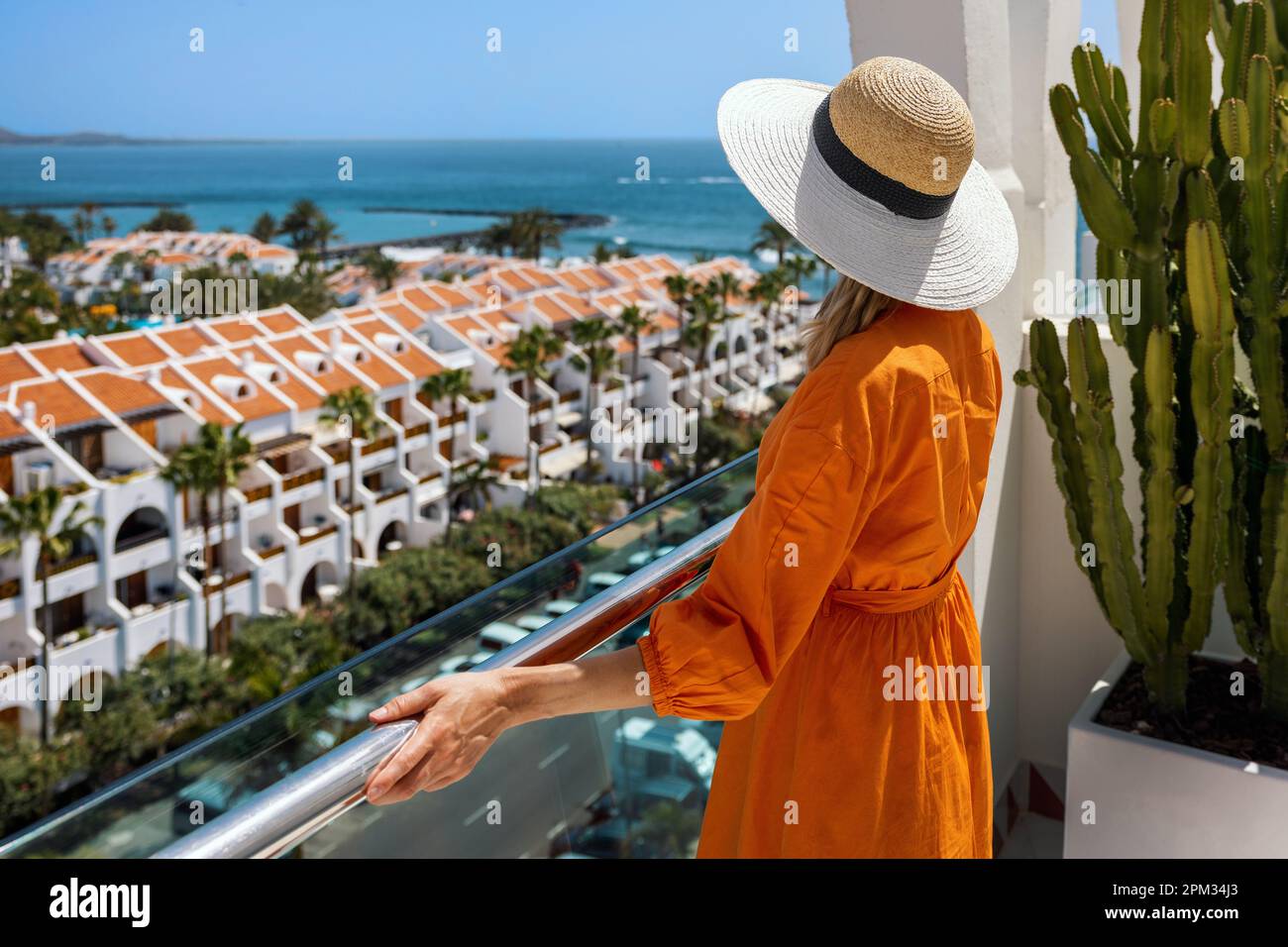 Frau steht auf dem Balkon und genießt den Blick auf das Playa de las Americas Resort auf Teneriffa. Sommerferien Stockfoto