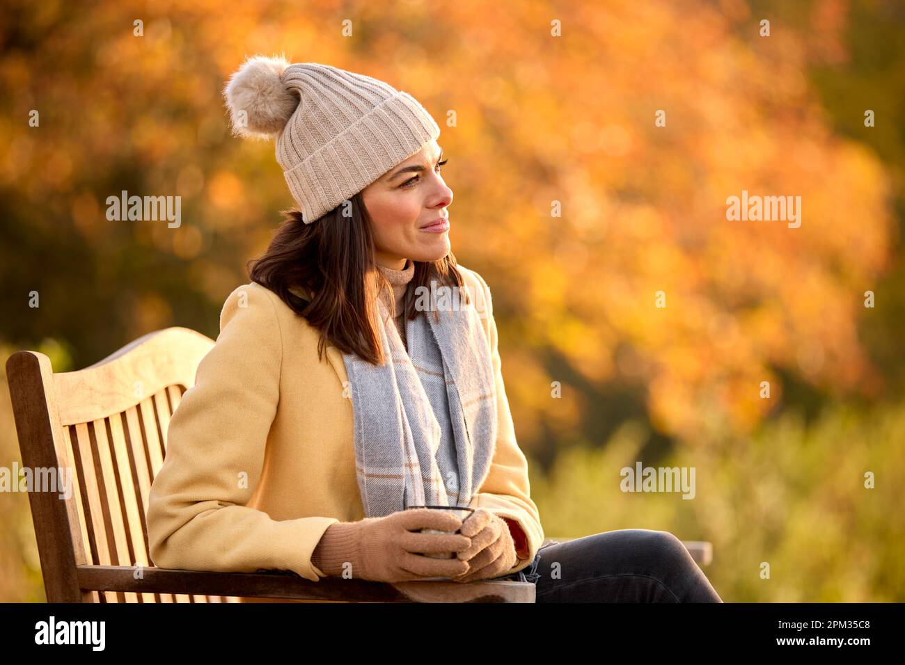 Frau Mit Hut Und Schal Mit Heißem Getränk Sitzt Auf Einer Bank Auf Einem Spaziergang In Der Herbstlandschaft Stockfoto