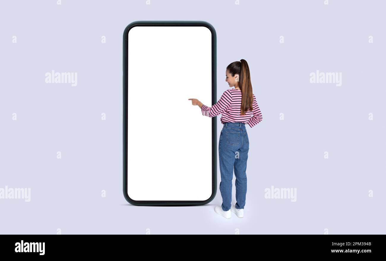 Junge, langhaarige Frau, die einen weißen Smartphone-Bildschirm berührt, Modell Stockfoto