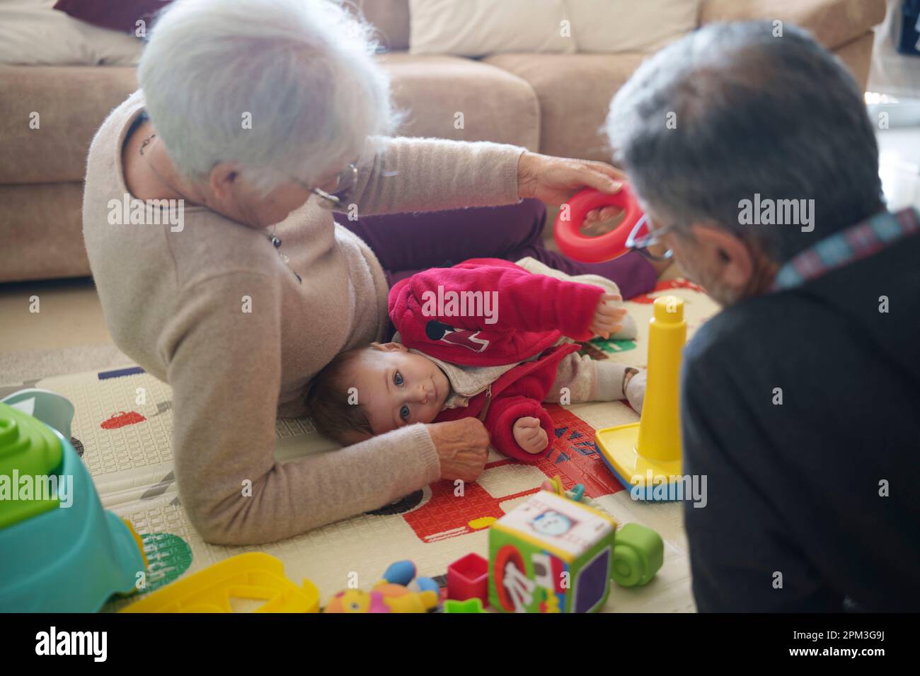 Ein kleiner Junge, der mit seinen Großeltern zu Hause auf dem Boden spielt Stockfoto