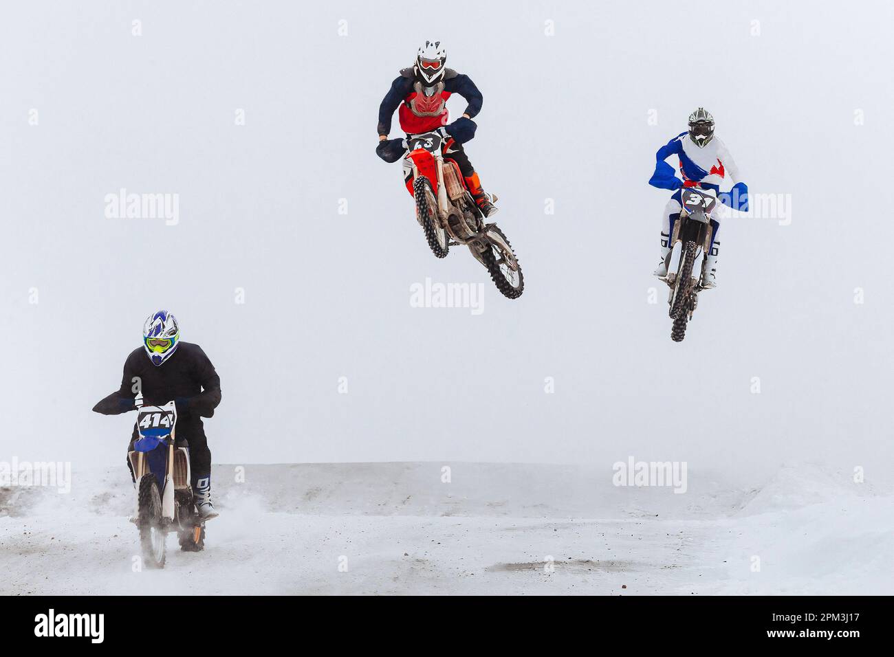 Motorsportfahrer, die gemeinsam auf einem verschneiten Sprungbrett springen, im Winter Off-Road-Motorradrennen Stockfoto