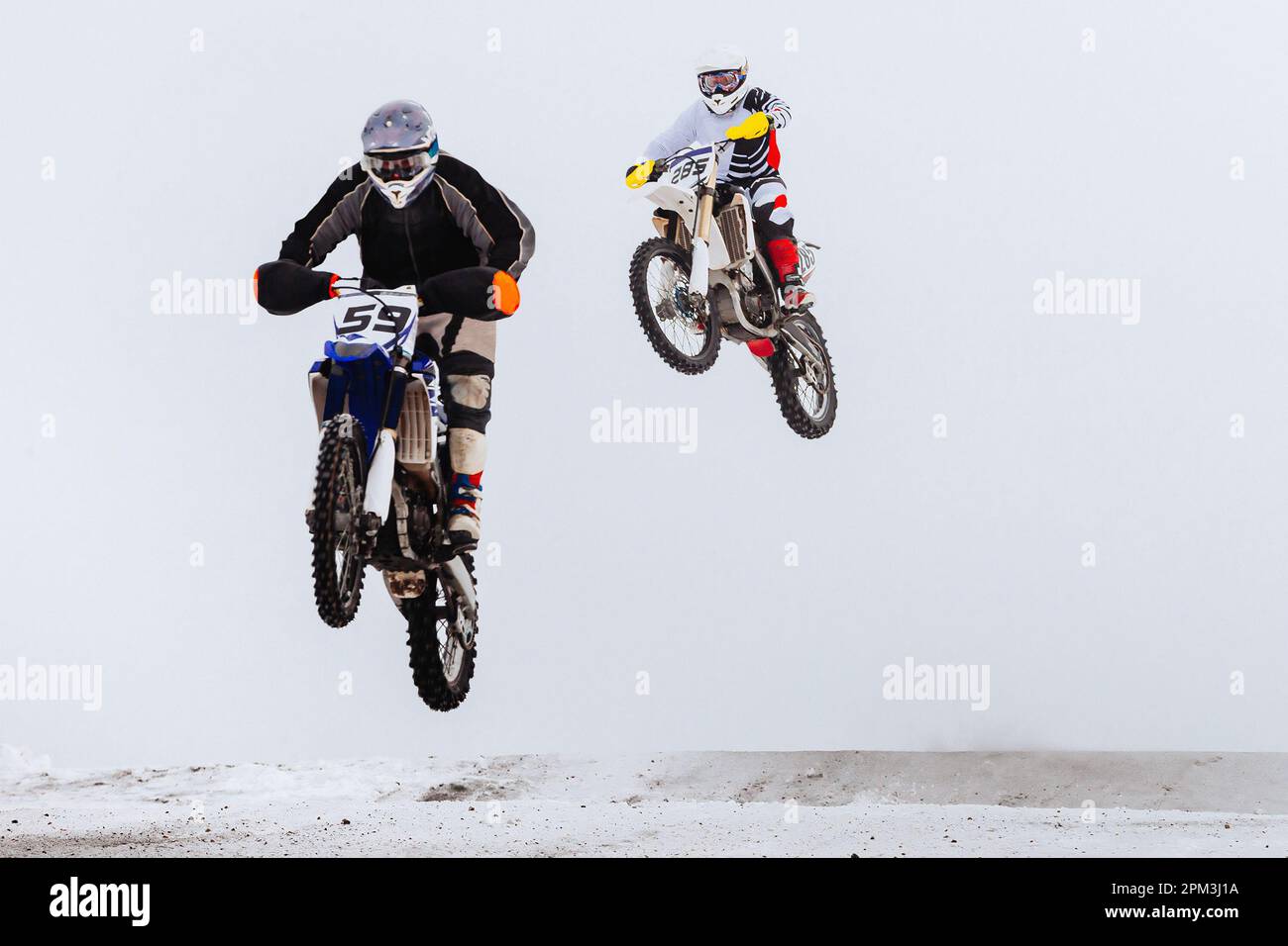 Zwei Motorsportfahrer, die gemeinsam auf einem verschneiten Sprungbrett springen, im Winter Off-Road-Motorradrennen Stockfoto