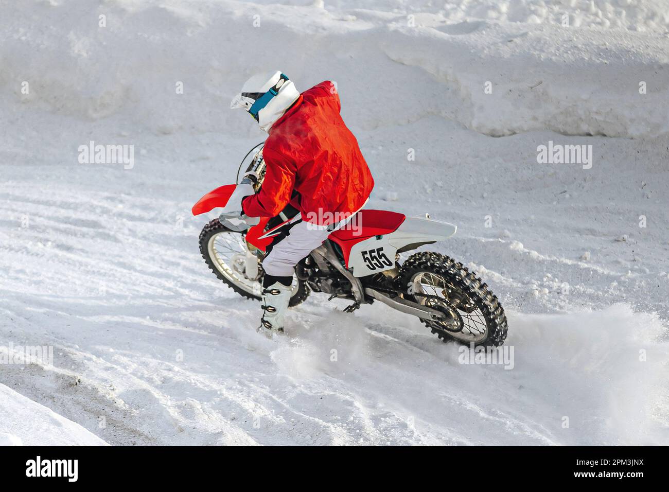 motocross-Fahrer, der im Winter Motorradrennen in scharfen Kurven fährt, Schnee spritzt unter dem Hinterrad Stockfoto