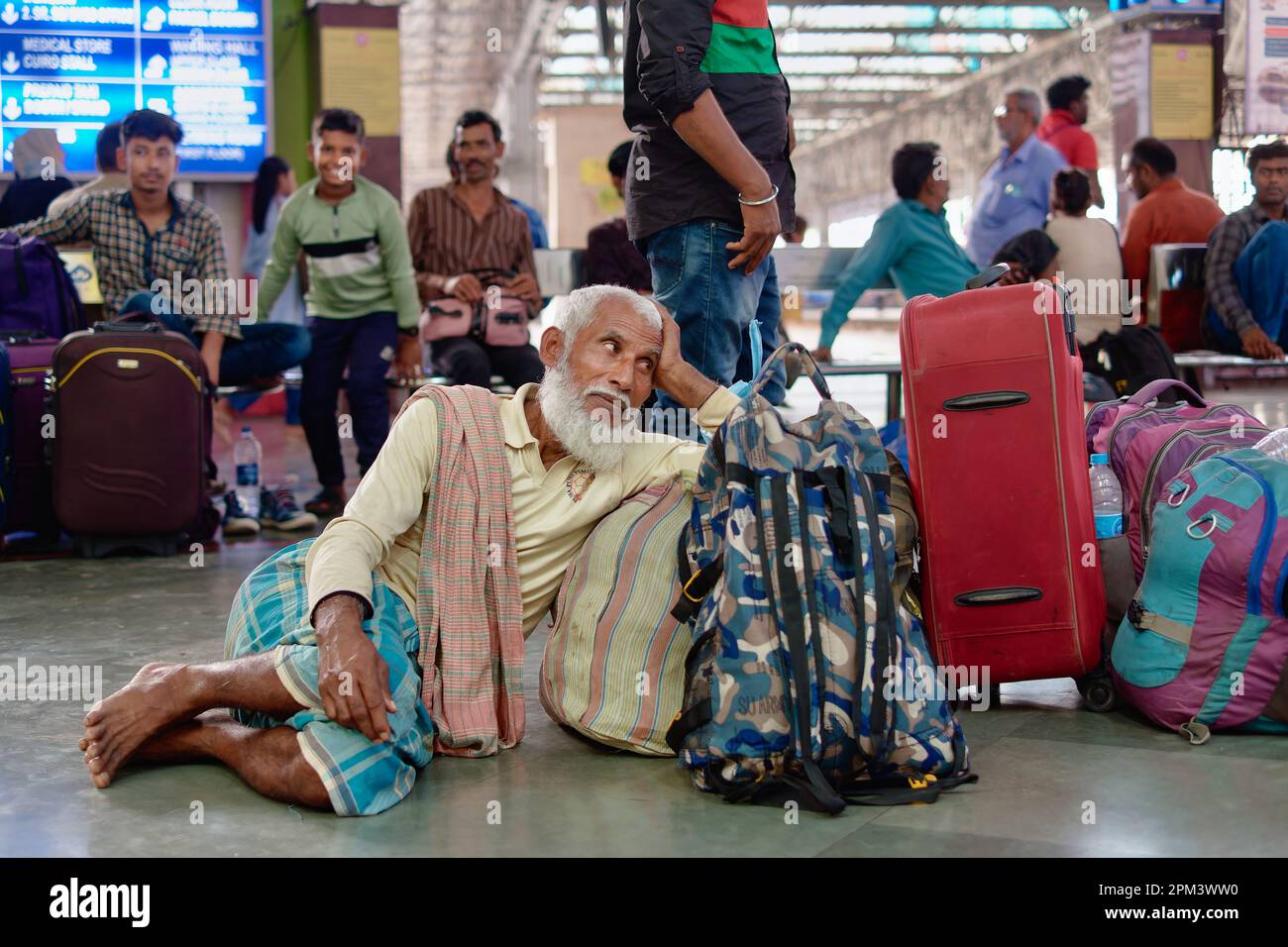 Ein bärtiger muslimischer Mann aus Kalkutta, der sich neben seinem Gepäck entspannt, während er auf seinen Zug wartet; Chhatrapati Shivaji Maharaj Terminus in Mumbai, Indien Stockfoto