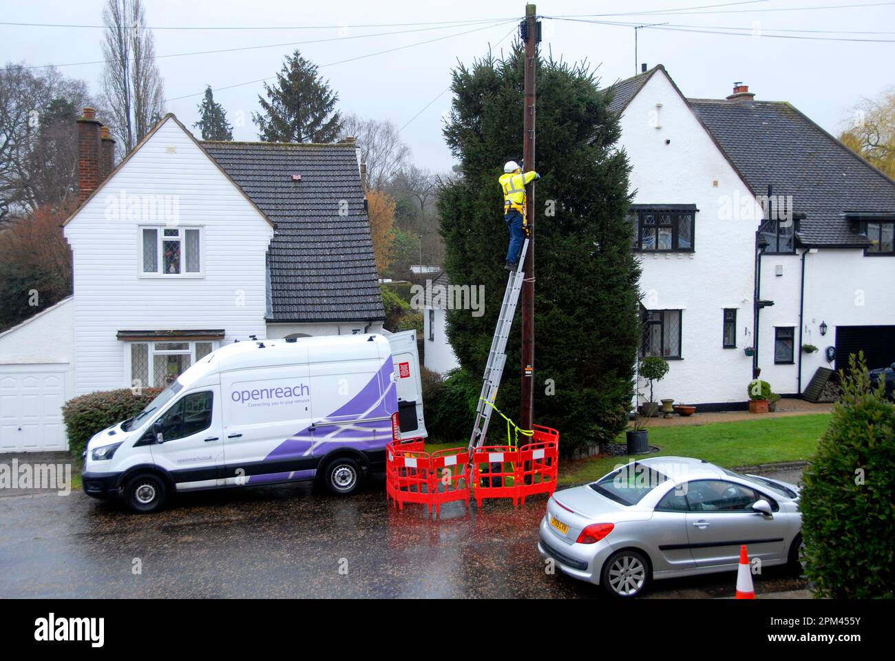 Arbeiter in gut sichtbarer gelber Jacke auf der Leiter, um bei nassem Wetter auf den Telegrafenmast zuzugreifen Stockfoto