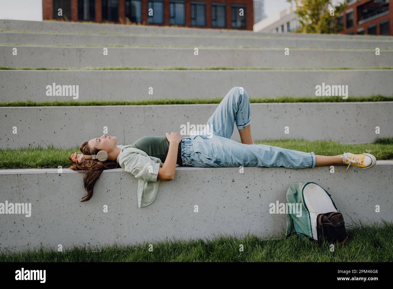 Junge Frau, die sich mit geschlossenen Augen im Stadtpark ausruhte und über Kopfhörer Musik genoss. Stockfoto
