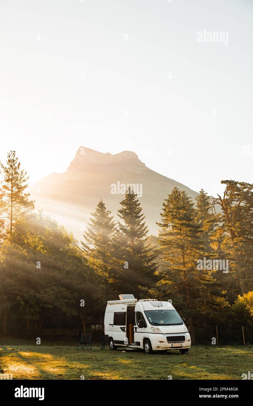 Wohnmobil in einem Tal mit herrlicher Aussicht auf Wald, Berge und Sonnenschein bei Sonnenaufgang. Roadtrip im Minibus und Sommerabenteuer im Freien Stockfoto