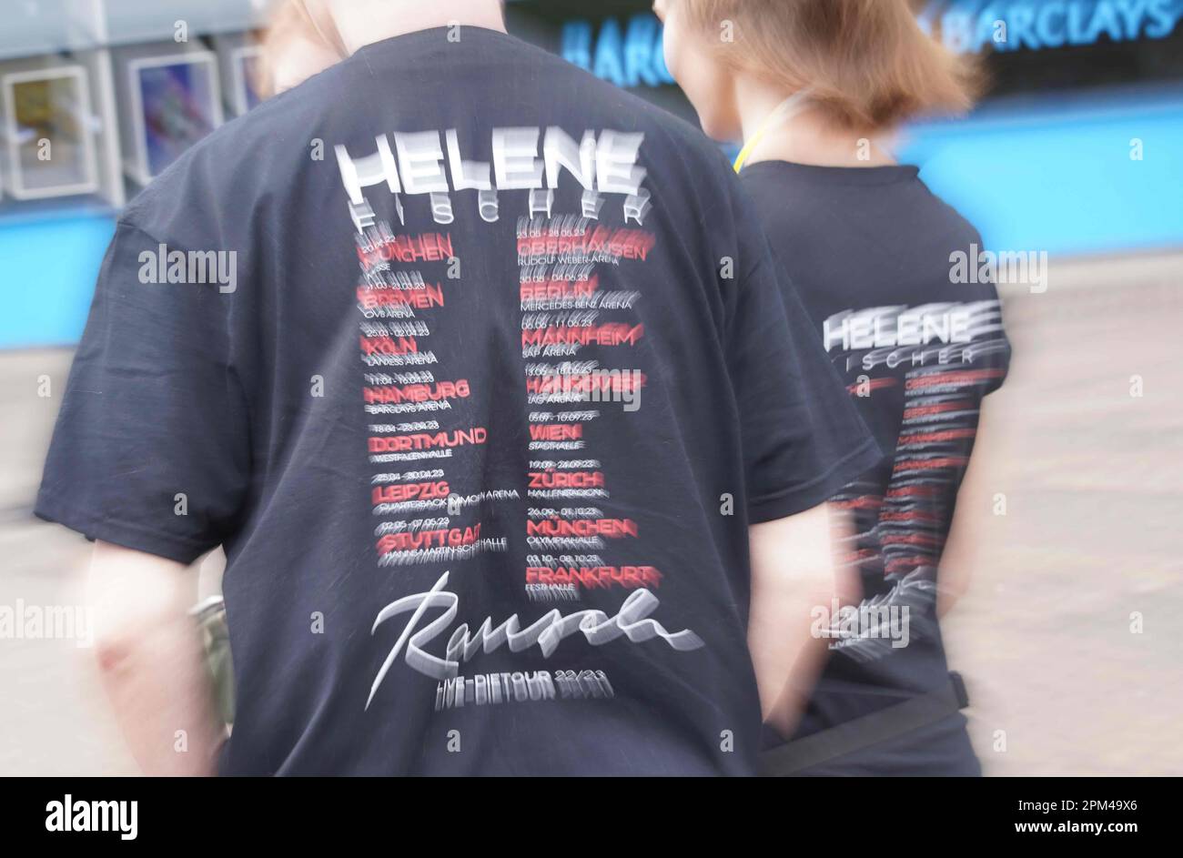Hamburg, Deutschland. 11. April 2023. Mit Helene Fischer T-Shirts, auf denen die Termine aller Konzerte der Tour „Rausch“ auf der Rückseite zu lesen sind, stehen die Fans von Helene Fischer vor der Barclays Arena, wo die Sängerin Helene Fischer ihre Tour am Abend mit dem ersten von fünf Hamburger Konzerten beginnt. Der Sänger musste den Tourstart in Bremen und das Konzert in Köln wegen einer Rippenfraktur verschieben. Kredit: Marcus Brandt/dpa/Alamy Live News Stockfoto