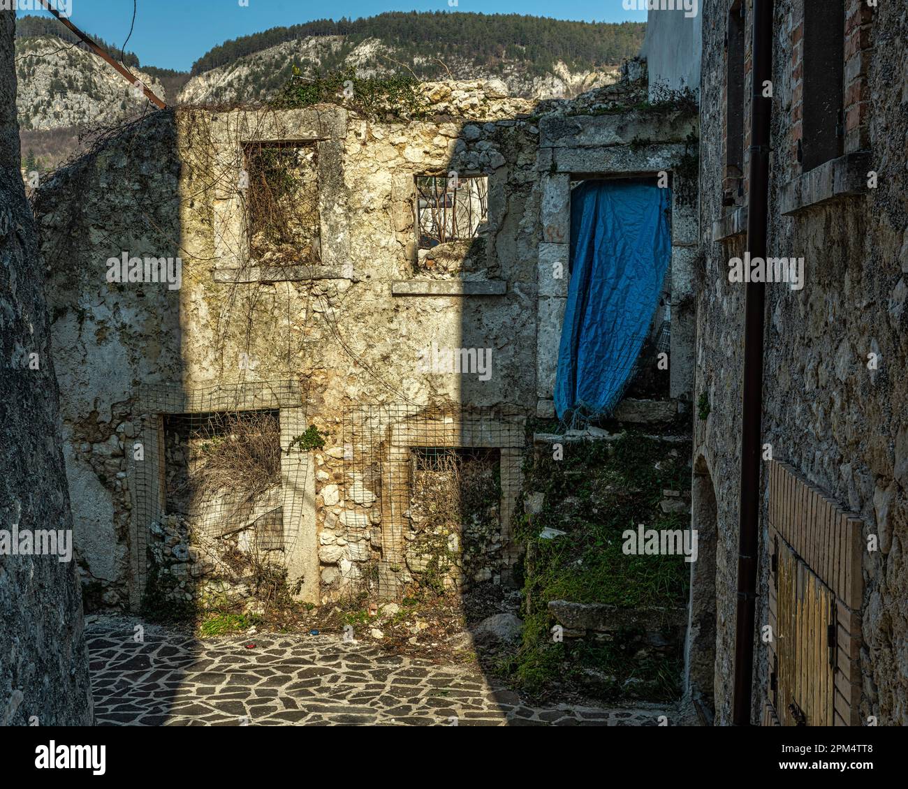 Überreste eines abgerissenen Hauses, von dem eine Wand mit Löchern in den Fenstern und Türen übrig bleibt. Schutt und Vegetation sind in das Haus eingedrungen. Abruzzen Stockfoto