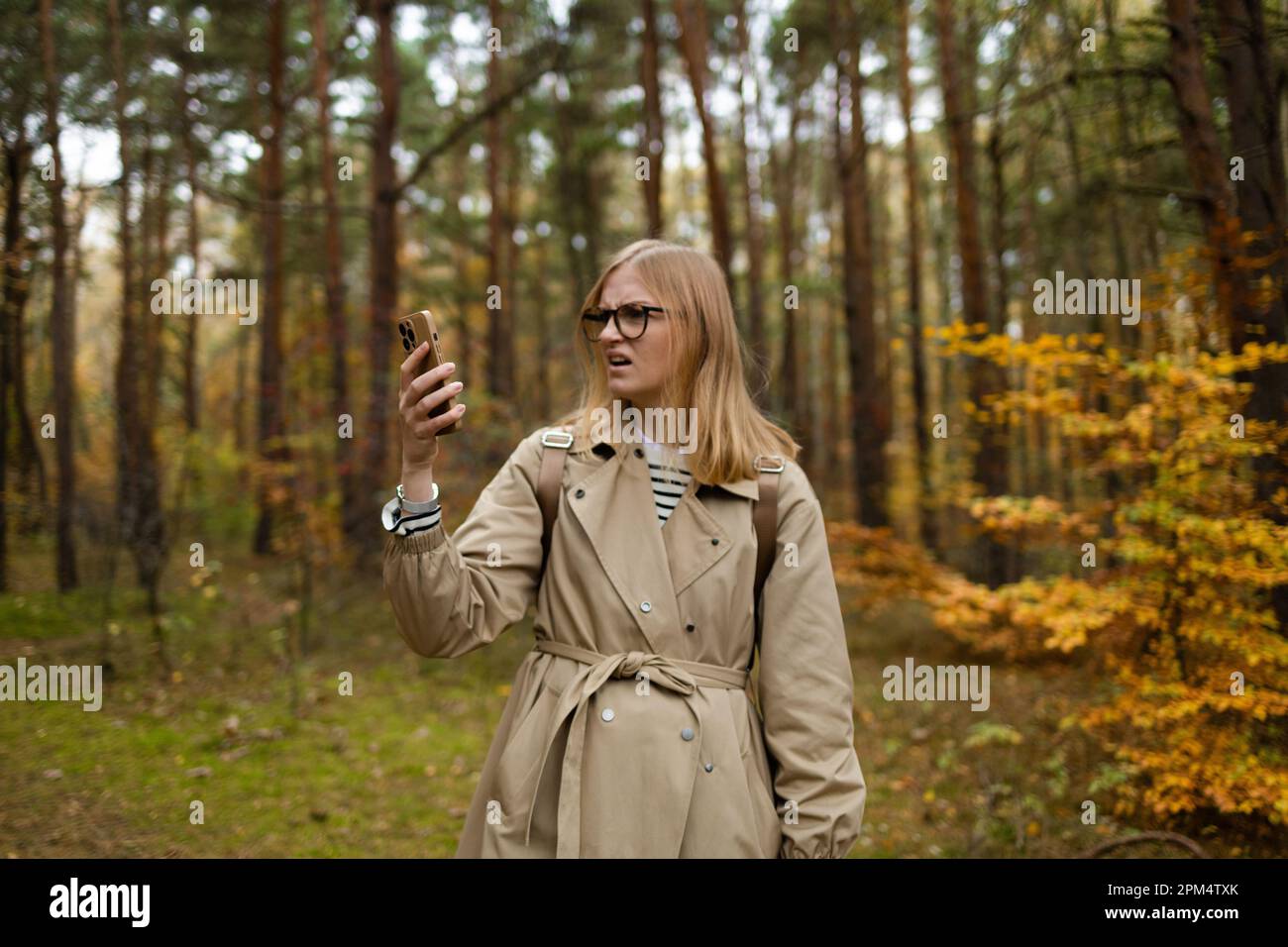 Eine Frau, die auf dem Mobiltelefon nach der Mobilfunkabdeckung sucht, steht in einem Herbstwald, ohne Service-Bildschirm Stockfoto