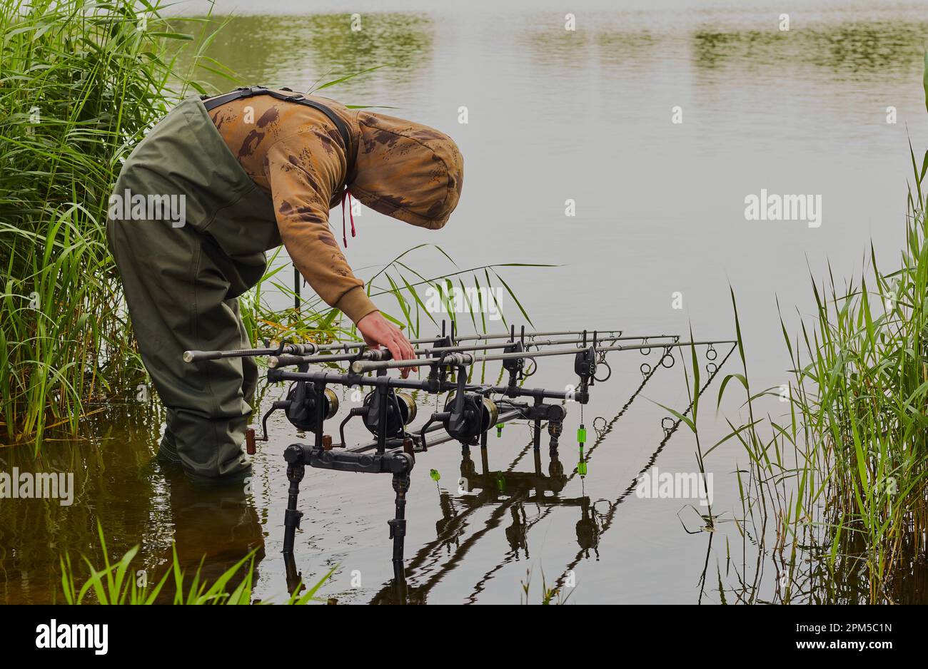 Fischer mit Wadern, die sich über die Rute und Rollen im Wasser gebeugt haben. Stockfoto