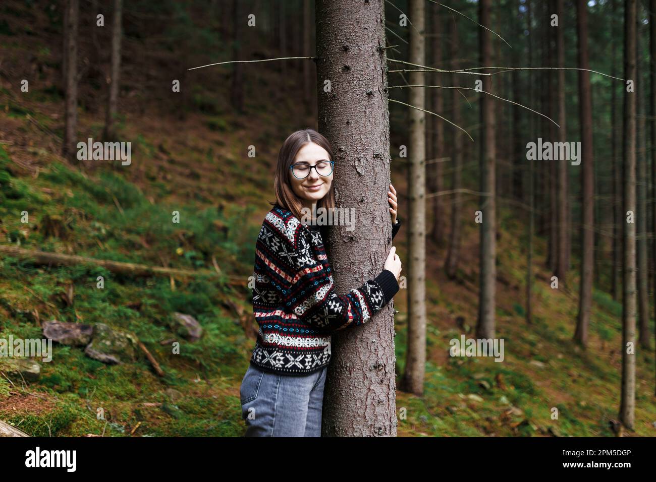 Eine Frau, die die Natur im Wald genießt und allein in Stille einen Baumstamm umarmt Stockfoto