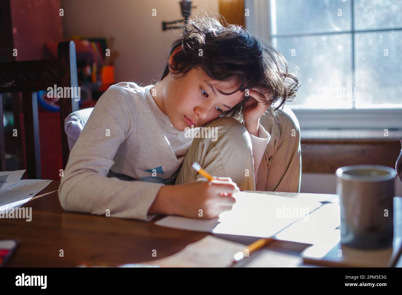 Ein Kind mit Kopf in den Händen konzentriert sich auf die Hausarbeit Stockfoto