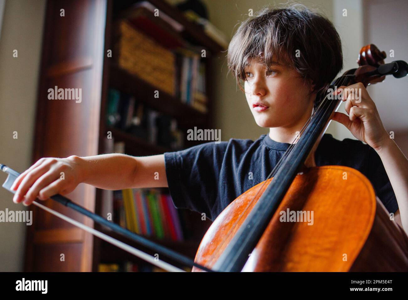 Nahaufnahme eines schweren Kindes, das Cello im Fensterlicht praktiziert Stockfoto
