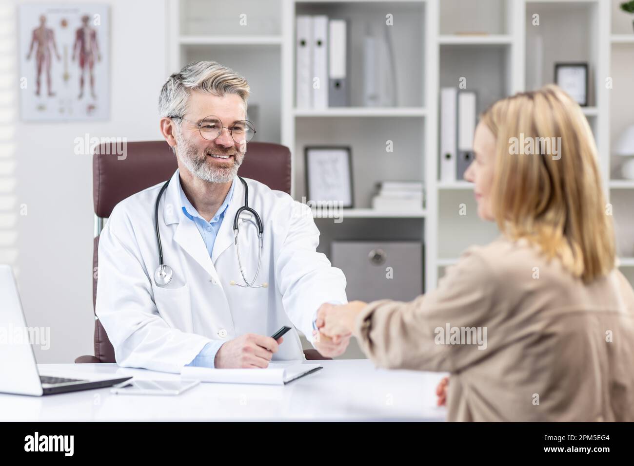 rztliche Beratung beim Arzt, der Patient schttelt die Hand des Arztes mit  Befriedigung, ein reifer Arzt in einem weien Kittel lchelt in der  Sprechstunde zu arbeiten Stockfotografie - Alamy
