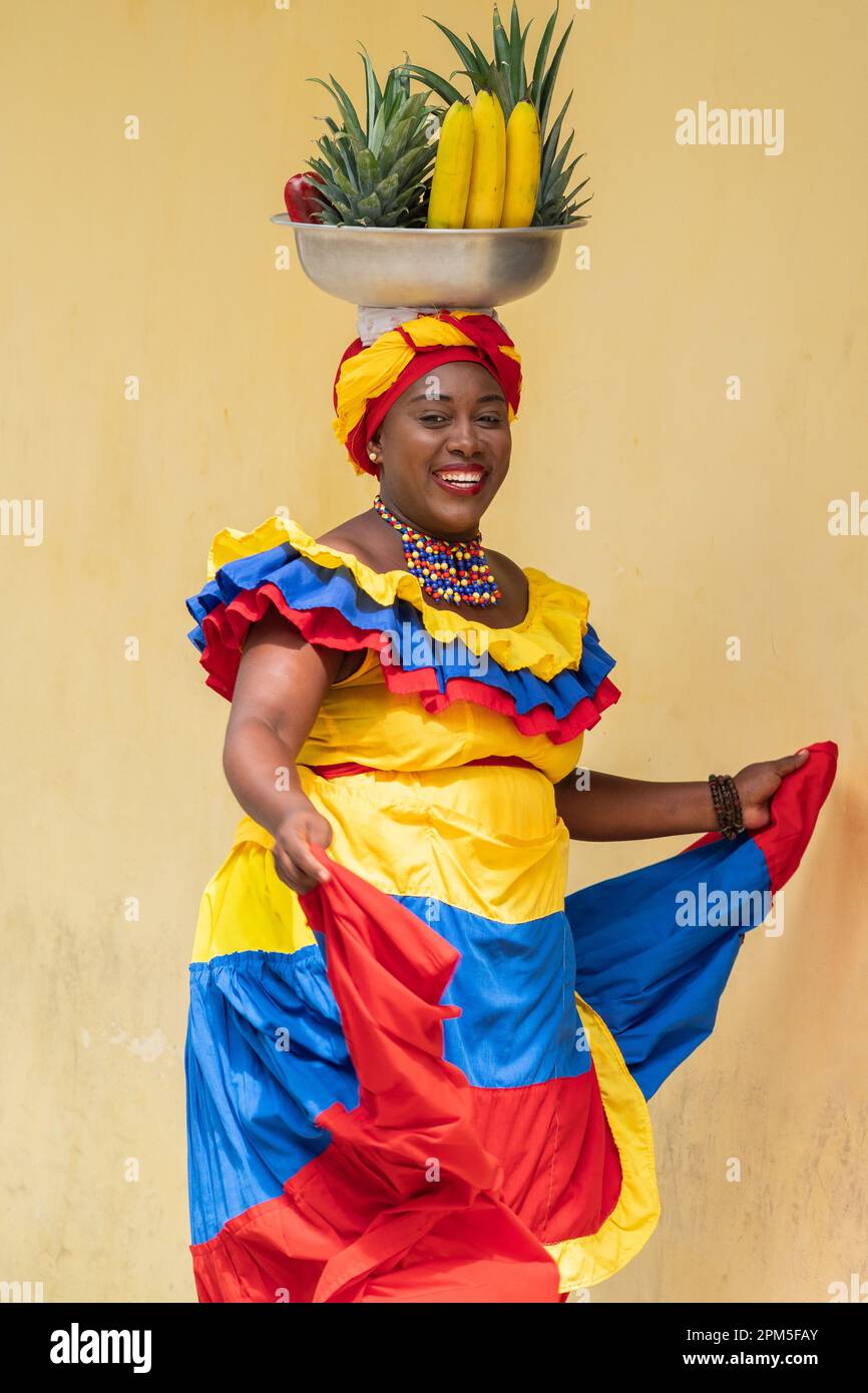 Fröhlich lächelnder Straßenverkäufer aus frischem Obst in Palenquera, der in Cartagena de Indias, Kolumbien, tanzt. Fröhliche afrokolumbianische Frau in traditionellen Kostümen. Stockfoto