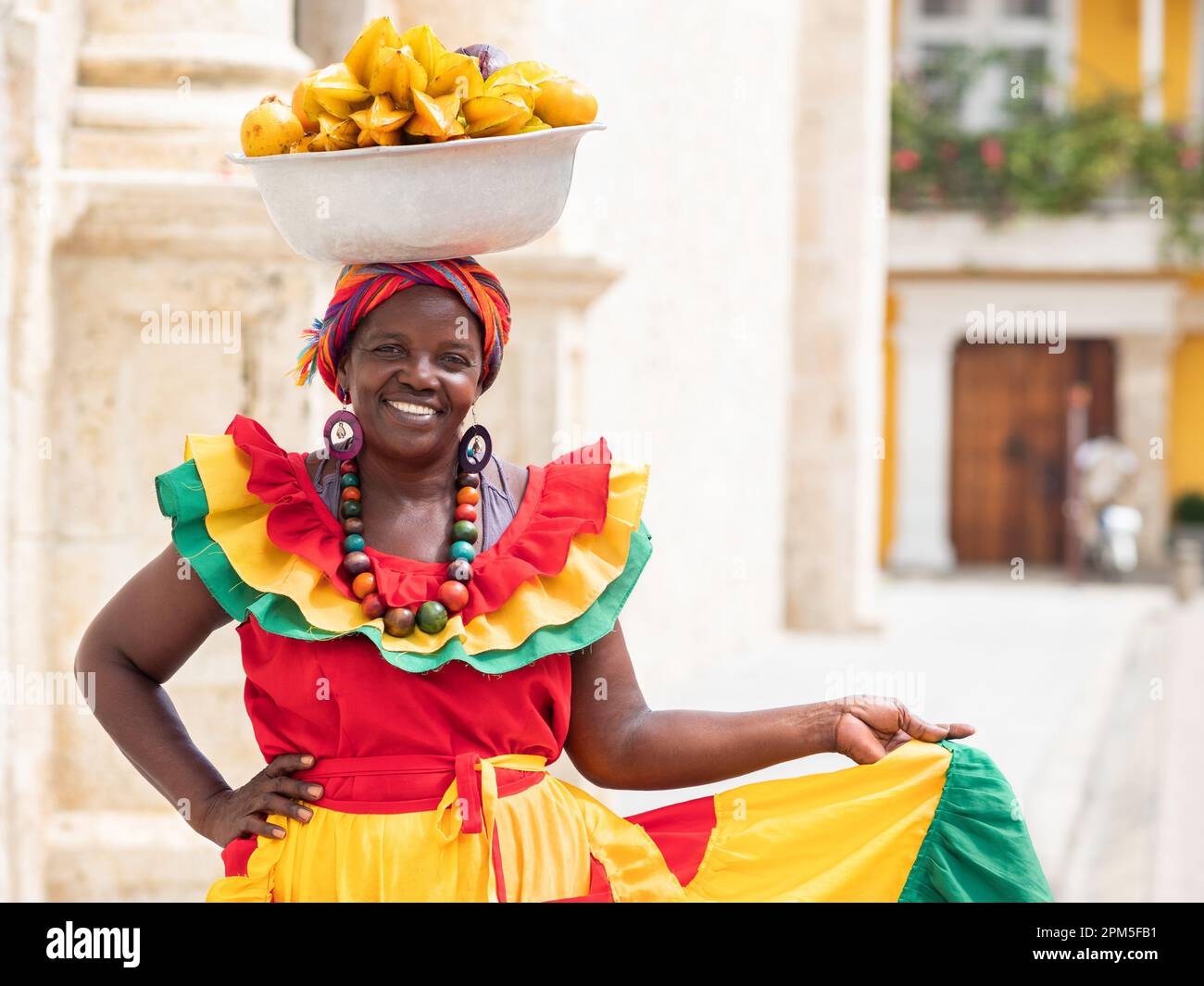 Fröhlicher, lächelnder Palenquera-Straßenverkäufer mit frischem Obst in der Altstadt von Cartagena, Kolumbien. Fröhliche afrokolumbianische Frau in traditionellen Kostümen. Stockfoto