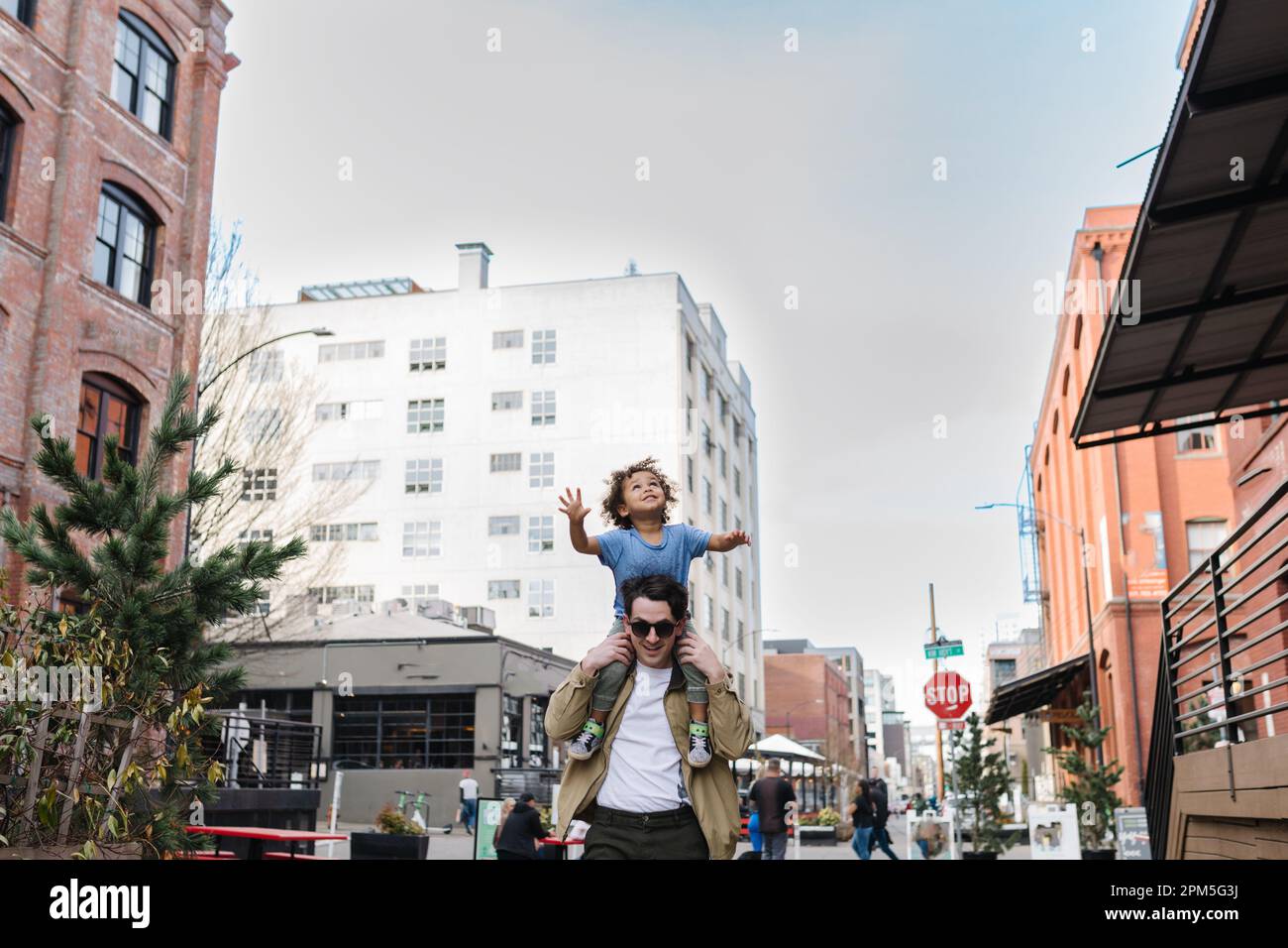 Dad trägt ein glückliches birassisches Kleinkind auf den Schultern in der Stadt Stockfoto