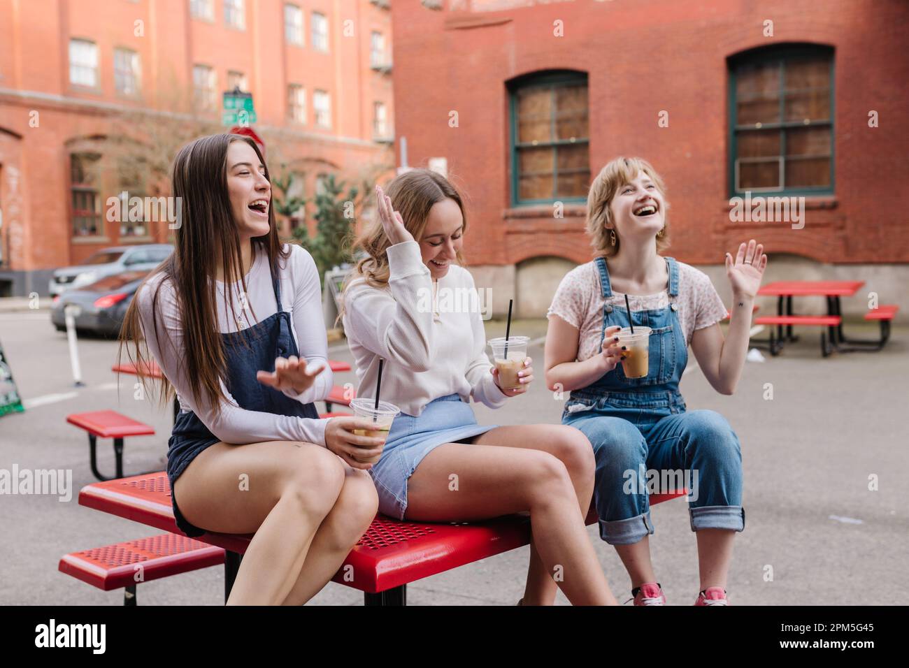 Freundinnen lachen, während sie auf einem Tisch im Innenhof sitzen Stockfoto
