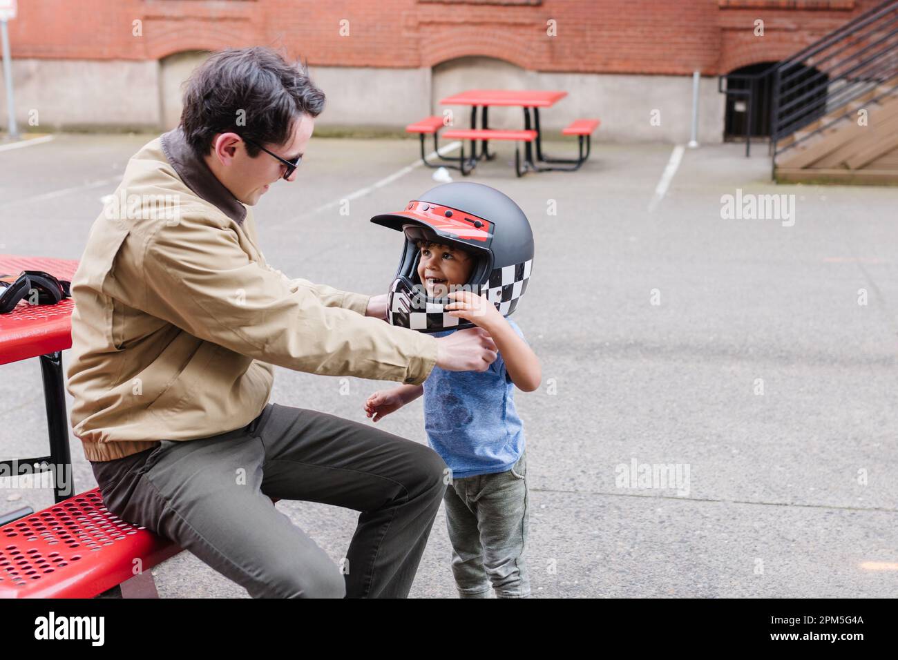 Lächelnder Mann, der einem Kleinkind hilft, den Motorradhelm draußen aufzusetzen Stockfoto