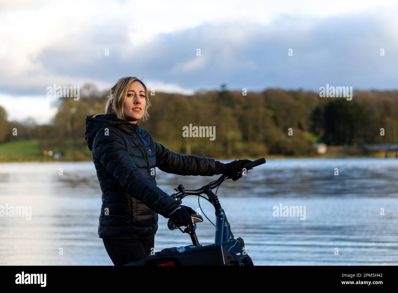 Eine junge Frau, die in die Kamera schaut und ihr Fahrrad hält Stockfoto