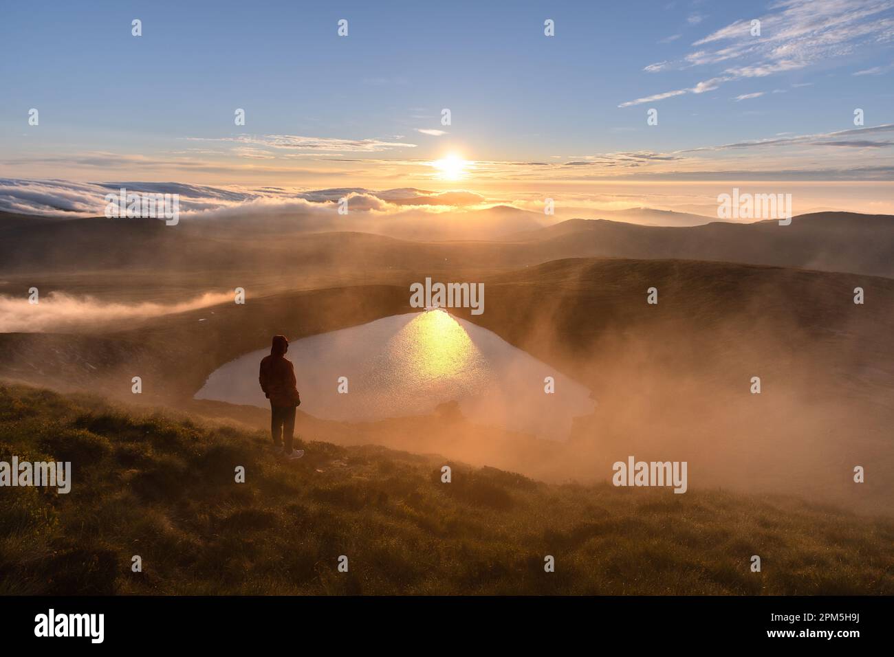 Ein Mann, der den Sonnenaufgang über einem herzförmigen See beobachtet Stockfoto