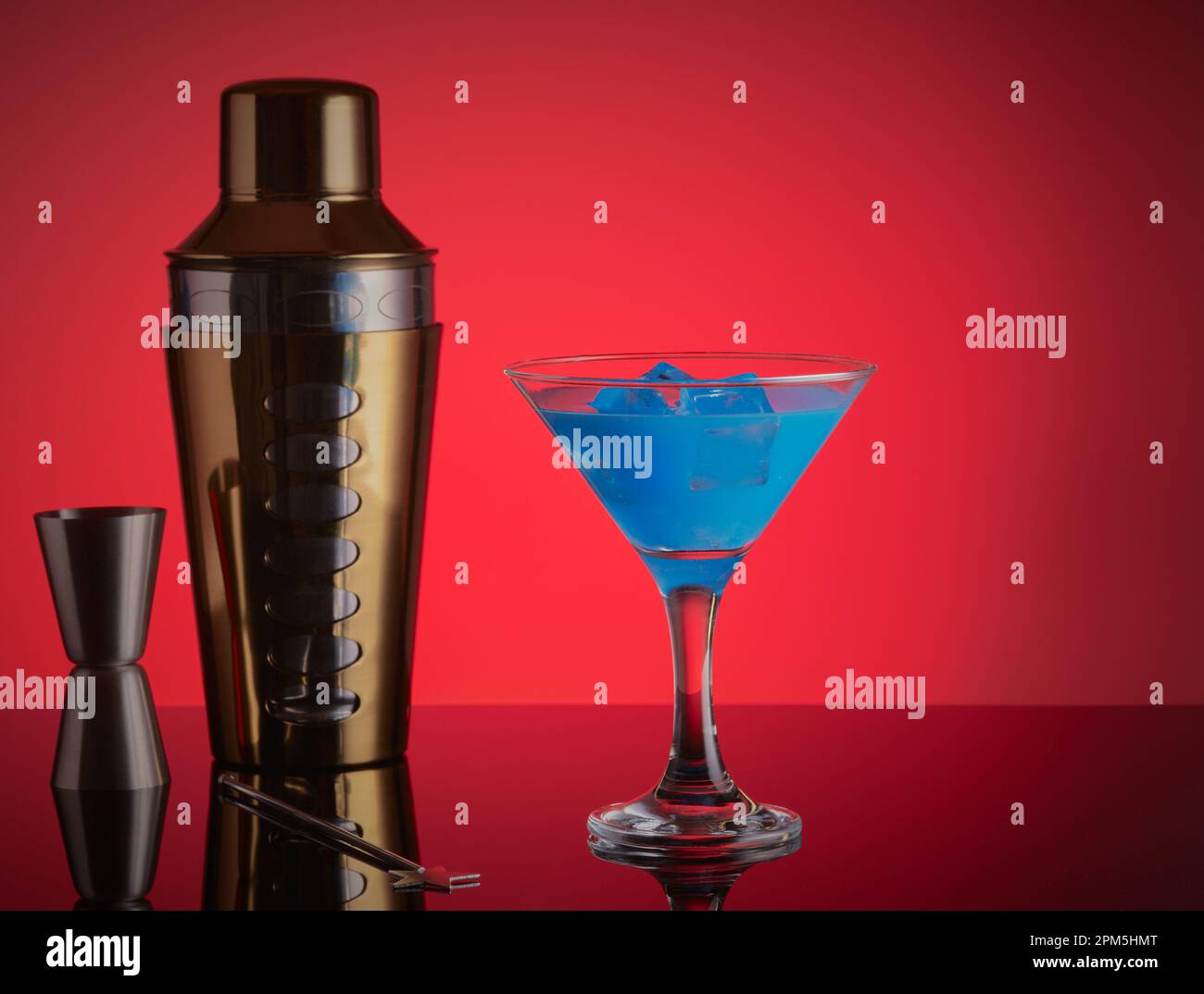 Blauer Cocktail mit Cocktail-Shaker und seitlich mit rotem Hintergrund messen Stockfoto