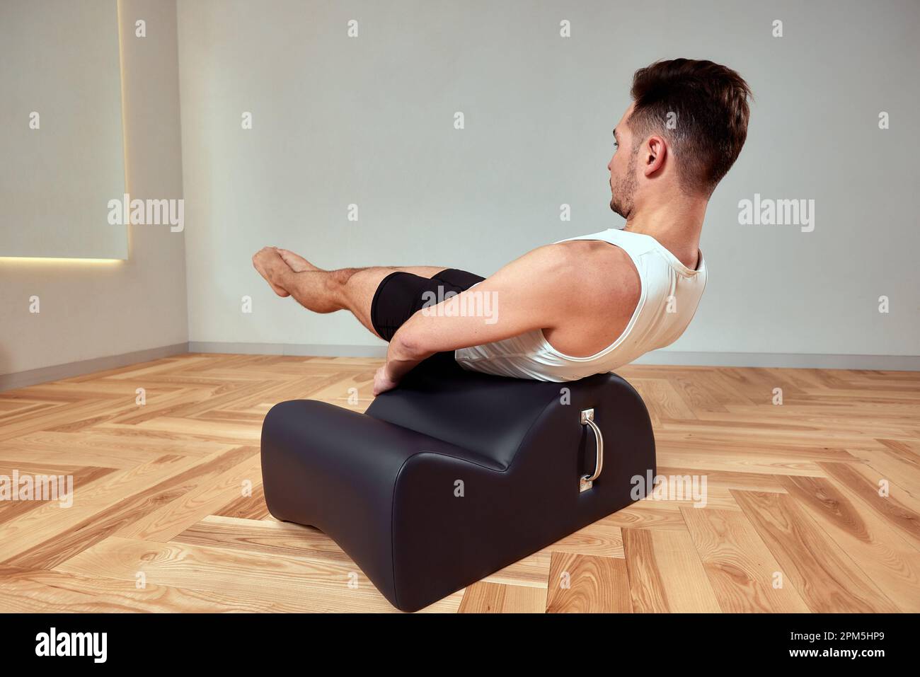 Ein junger Mann macht Pilates-Übungen auf einem Reformer, um die Beckenregion des Bewegungsapparates zu stärken, Pilates-Übungen auf Reformer. Kopieren en Stockfoto