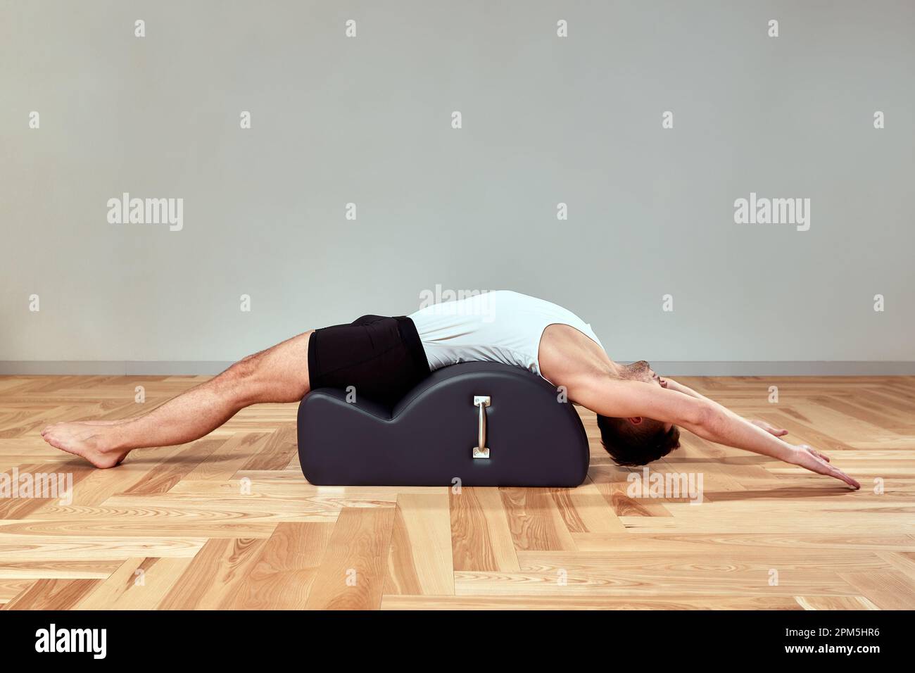 Ein junger Mann macht Pilates-Übungen auf einem Reformer, um die Beckenregion des Bewegungsapparates zu stärken, Pilates-Übungen auf Reformer. Kopieren en Stockfoto