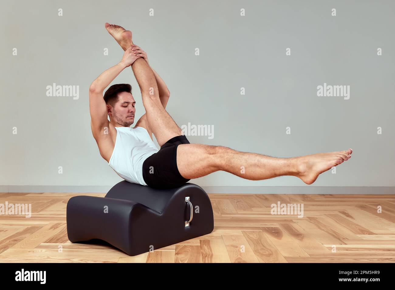 Ein junger Mann macht Pilates-Übungen auf einem Reformer, um die Beckenregion des Bewegungsapparates zu stärken, Pilates-Übungen auf Reformer. Kopieren en Stockfoto