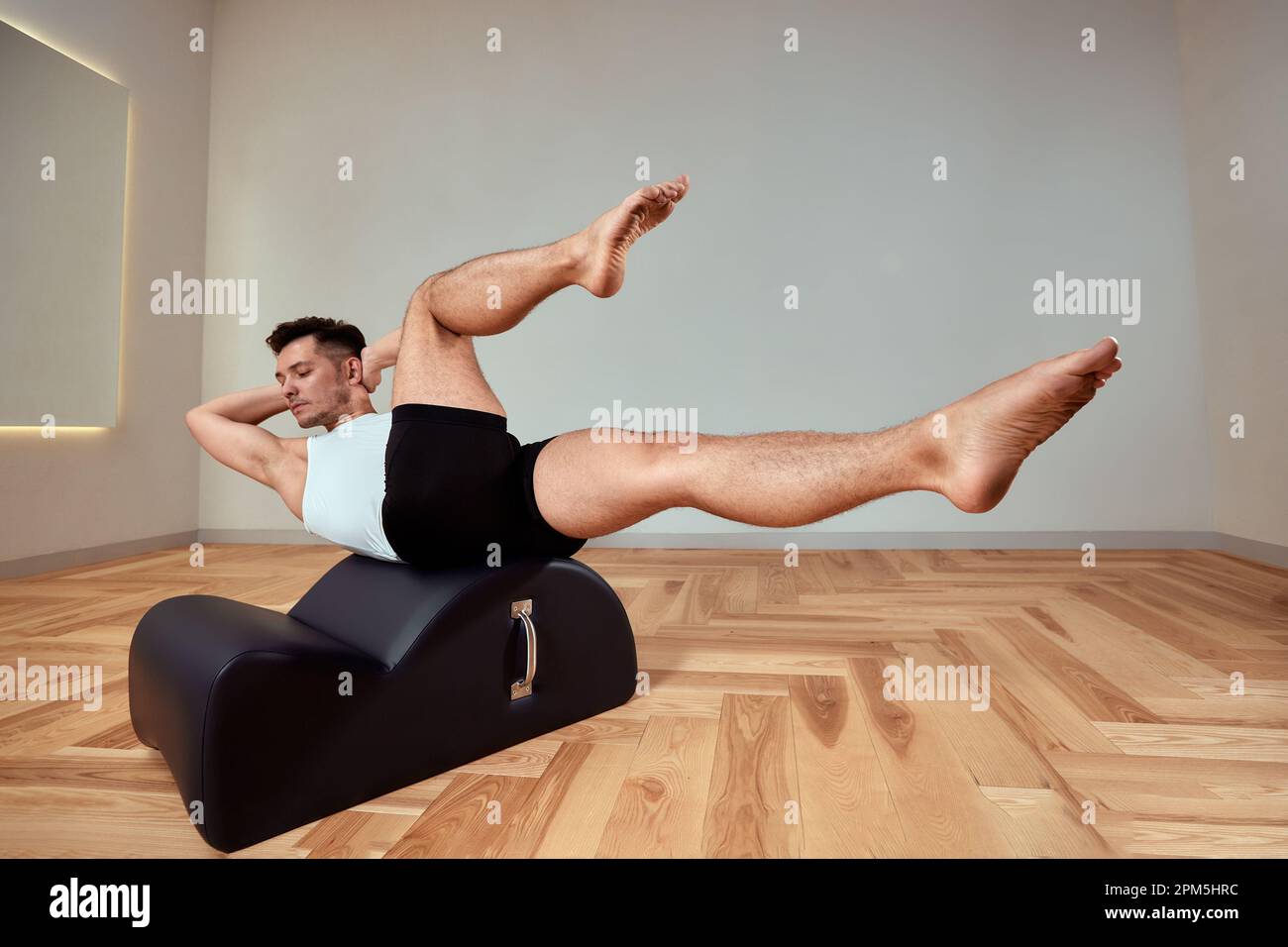 Ein junger Mann macht Pilates-Übungen auf einem Reformer, um die Beckenregion des Bewegungsapparates zu stärken, Pilates-Übungen auf Reformer. Kopieren en Stockfoto